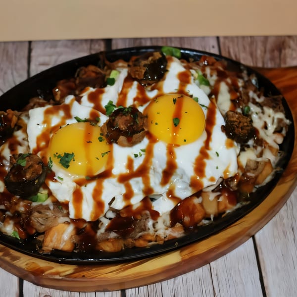 Water Street Waffle Co breakfast skillet with fried eggs, meat, cheese, and sauce on a wooden table.