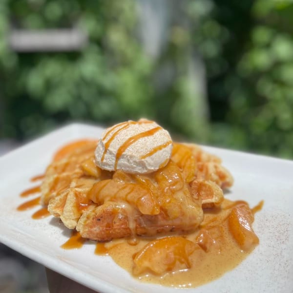 Water Street Waffle Co's apple pie waffle with whipped cream and caramel drizzle on a white plate.