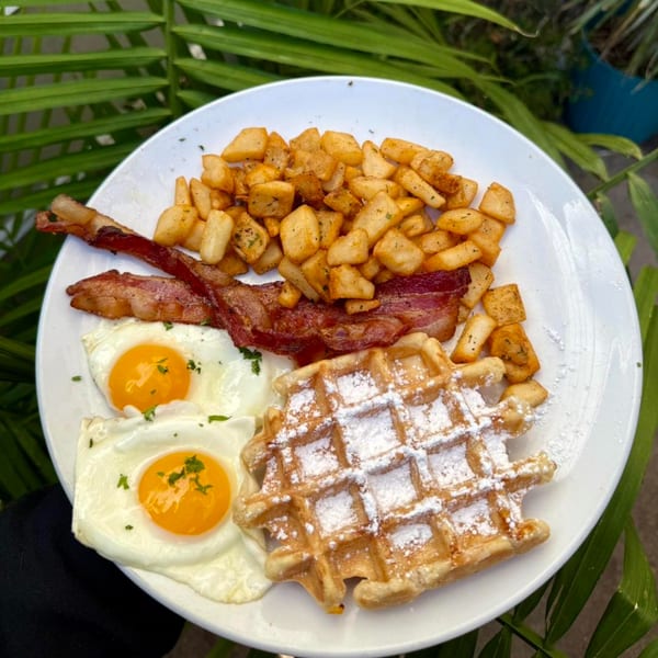 A Water Street Waffle Co. breakfast plate with a waffle, eggs, bacon, and home fries.