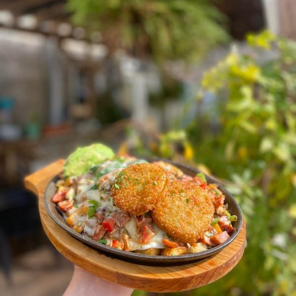 A breakfast skillet with hash browns, melted cheese, vegetables, and two crispy patties.