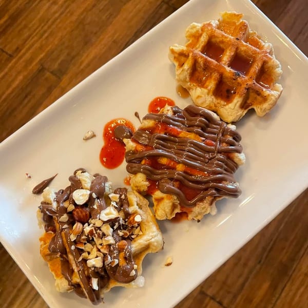 Three Water Street Waffle Co. waffles with various toppings on a white rectangular plate.