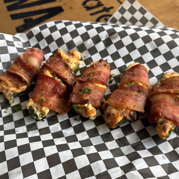 Bacon-wrapped jalapeño poppers with cheese filling, garnished with herbs, on checkered paper.