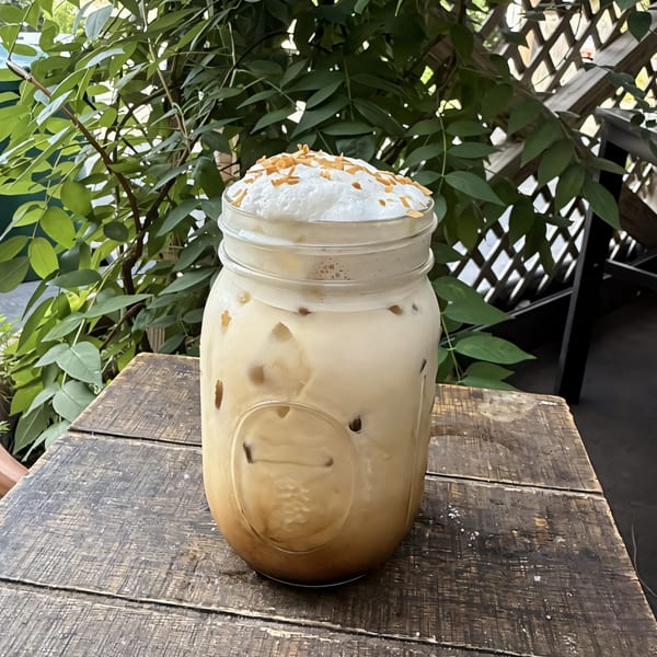 Iced coffee in a mason jar with whipped cream and caramel drizzle on a wooden table.