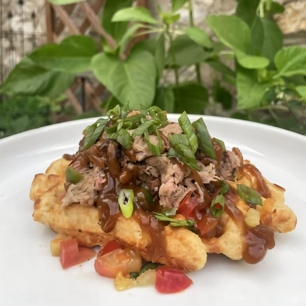 A Water Street Waffle Co. waffle topped with pulled pork, gravy, diced tomatoes, and green onions.